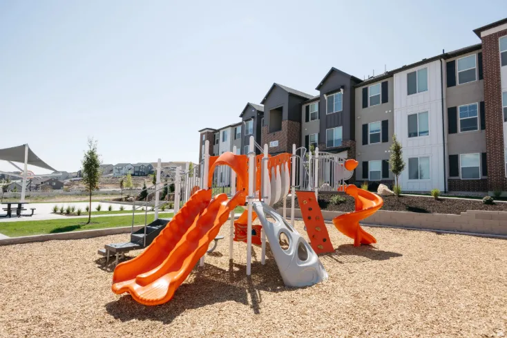 Outdoor playground with multiple slides and climbing features, situated on wood-chip ground cover