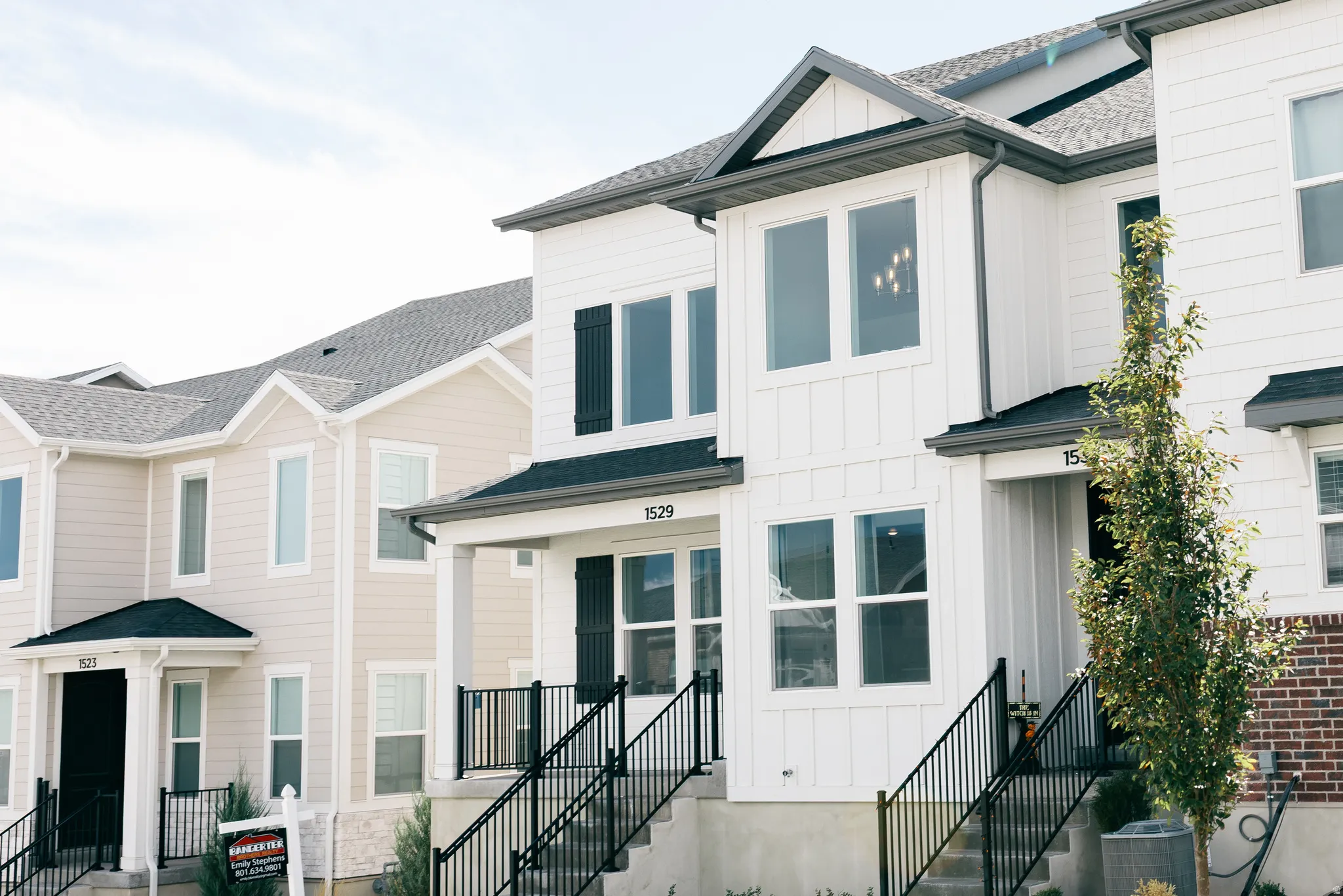 Contemporary townhome exterior featuring clean architectural lines, white siding, black window shutters, and a covered front entry