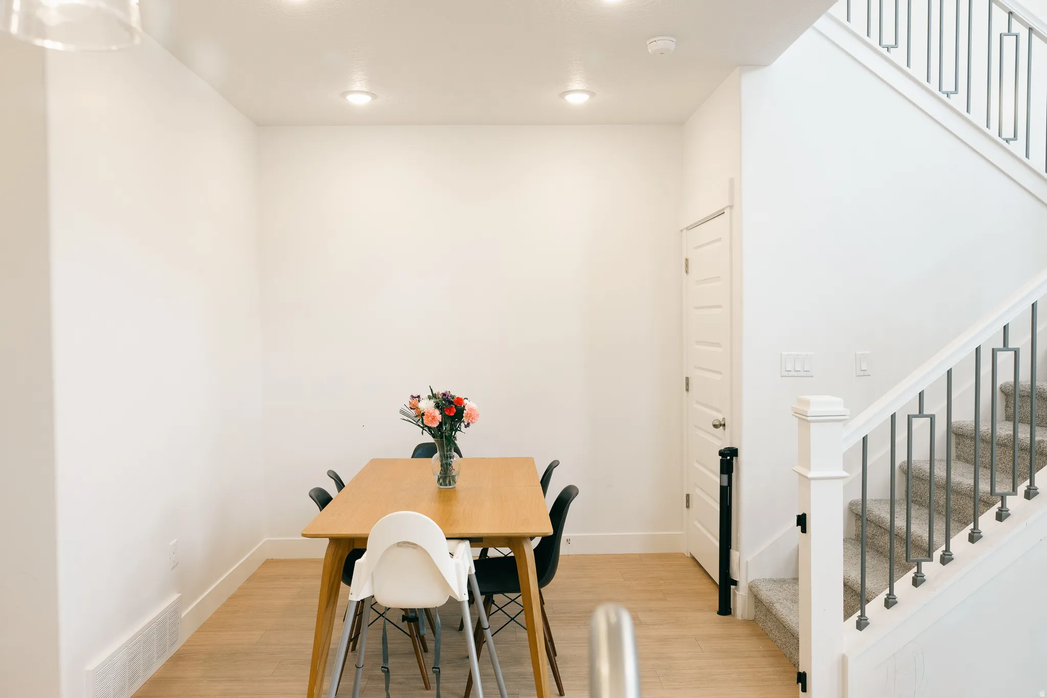 Recessed ceiling lighting illuminates the space, featuring wood-finish flooring, a paneled door, and a staircase with metal balusters