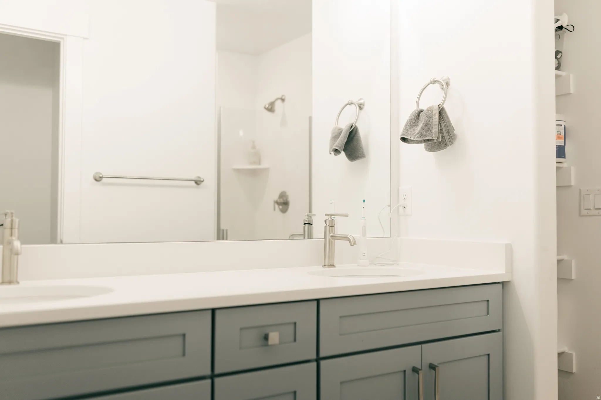 Double vanity with white countertop, undermount sinks, gray shaker-style cabinetry, and brushed nickel fixtures