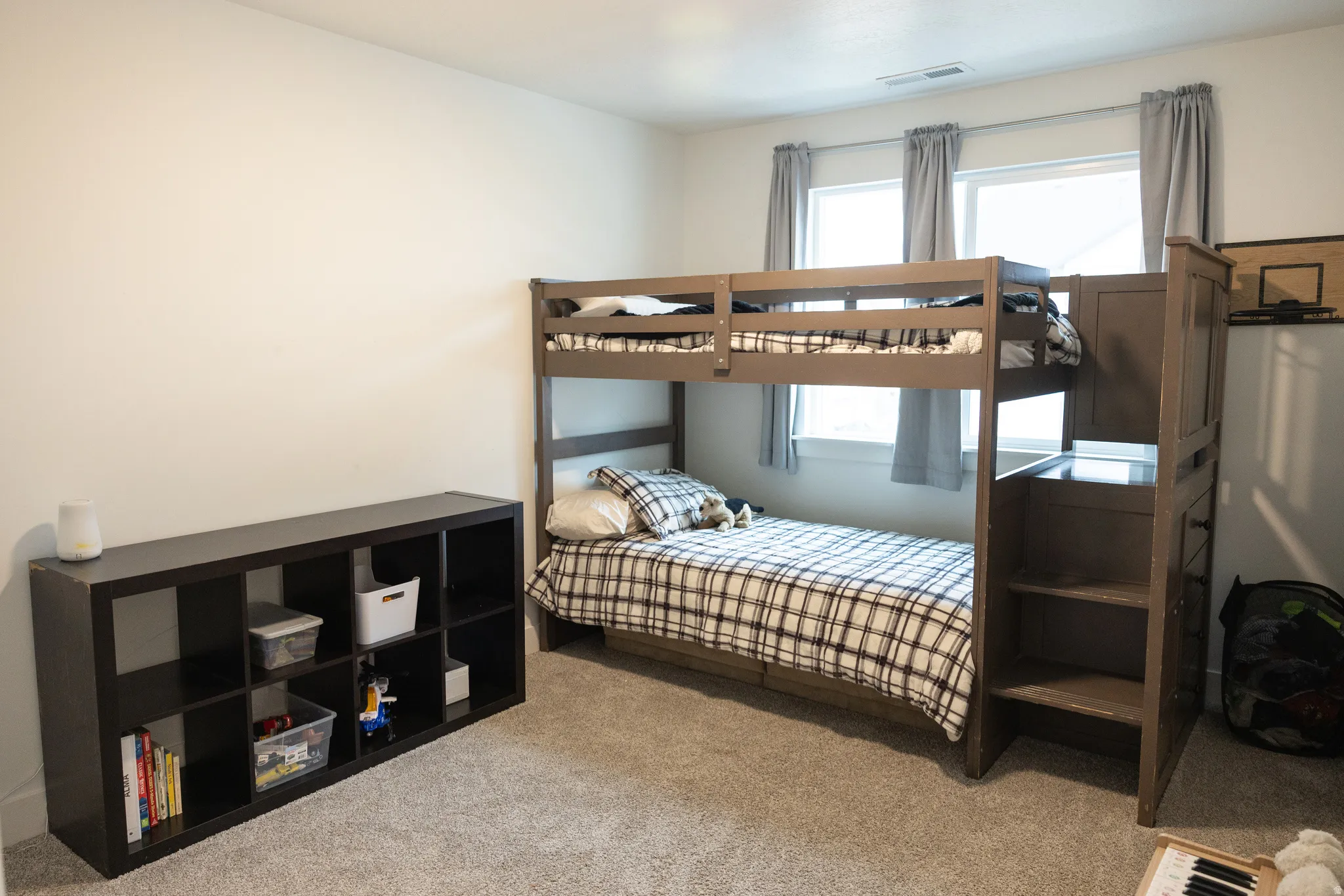 Carpeted room featuring bunk beds with integrated shelving and dual windows with window treatments