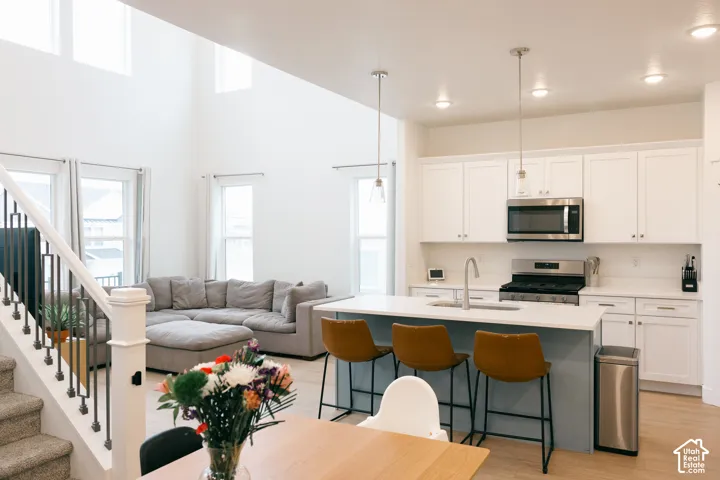Open-concept living area featuring a kitchen island with seating, stainless steel appliances, white cabinetry, and wood-finish flooring