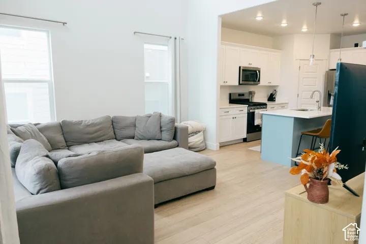 Recessed lighting, wood-finish flooring, white cabinetry, stainless steel appliances, and a kitchen island with pendant lighting