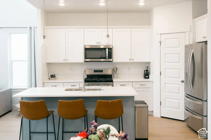 Kitchen featuring white cabinetry, stainless steel appliances, a center island with sink, light wood-finish flooring, and recessed lighting