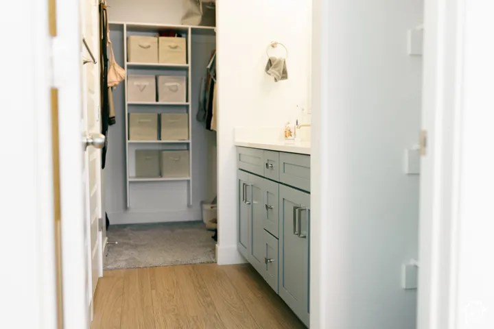Wood-finish flooring, built-in closet shelving system, light gray cabinetry, wall-mounted faucet, and a clean white countertop