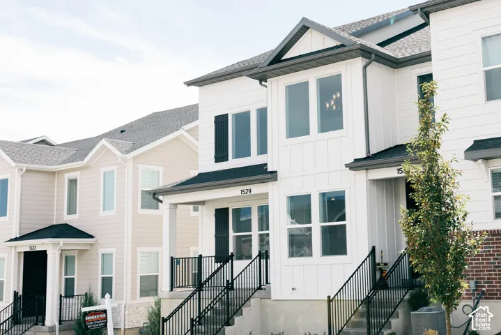 Contemporary townhome exterior featuring clean architectural lines, white siding, black window shutters, and a covered front entry