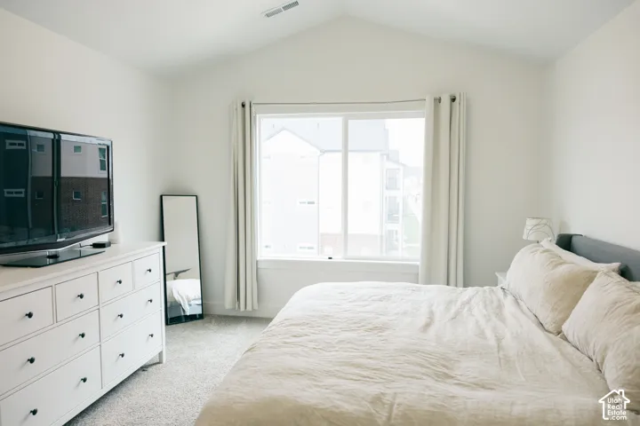 Vaulted ceiling with a large window, light-colored walls, and carpet flooring