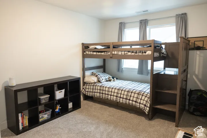 Carpeted room featuring bunk beds with integrated shelving and dual windows with window treatments