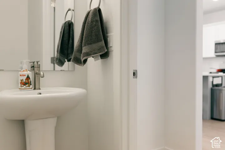 Pedestal sink with a brushed nickel faucet, wall-mounted mirror, and wood-finish flooring