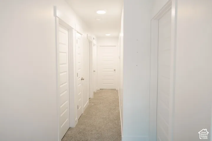 Hallway with recessed lighting, white paneled doors, and light-colored carpeting