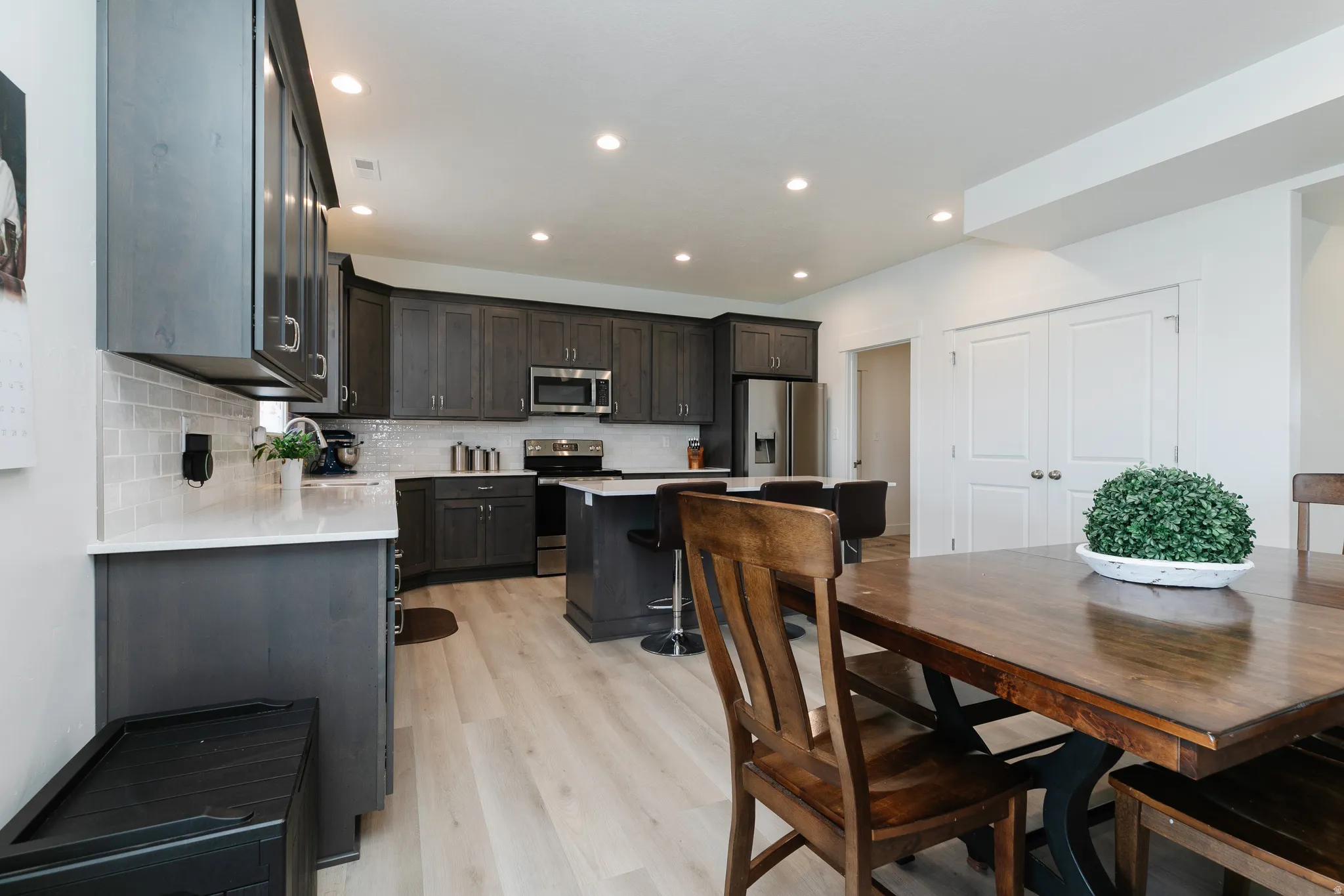 Open kitchen featuring dark wood-finish cabinetry, light stone countertops, stainless steel appliances, and a subway tile backsplash