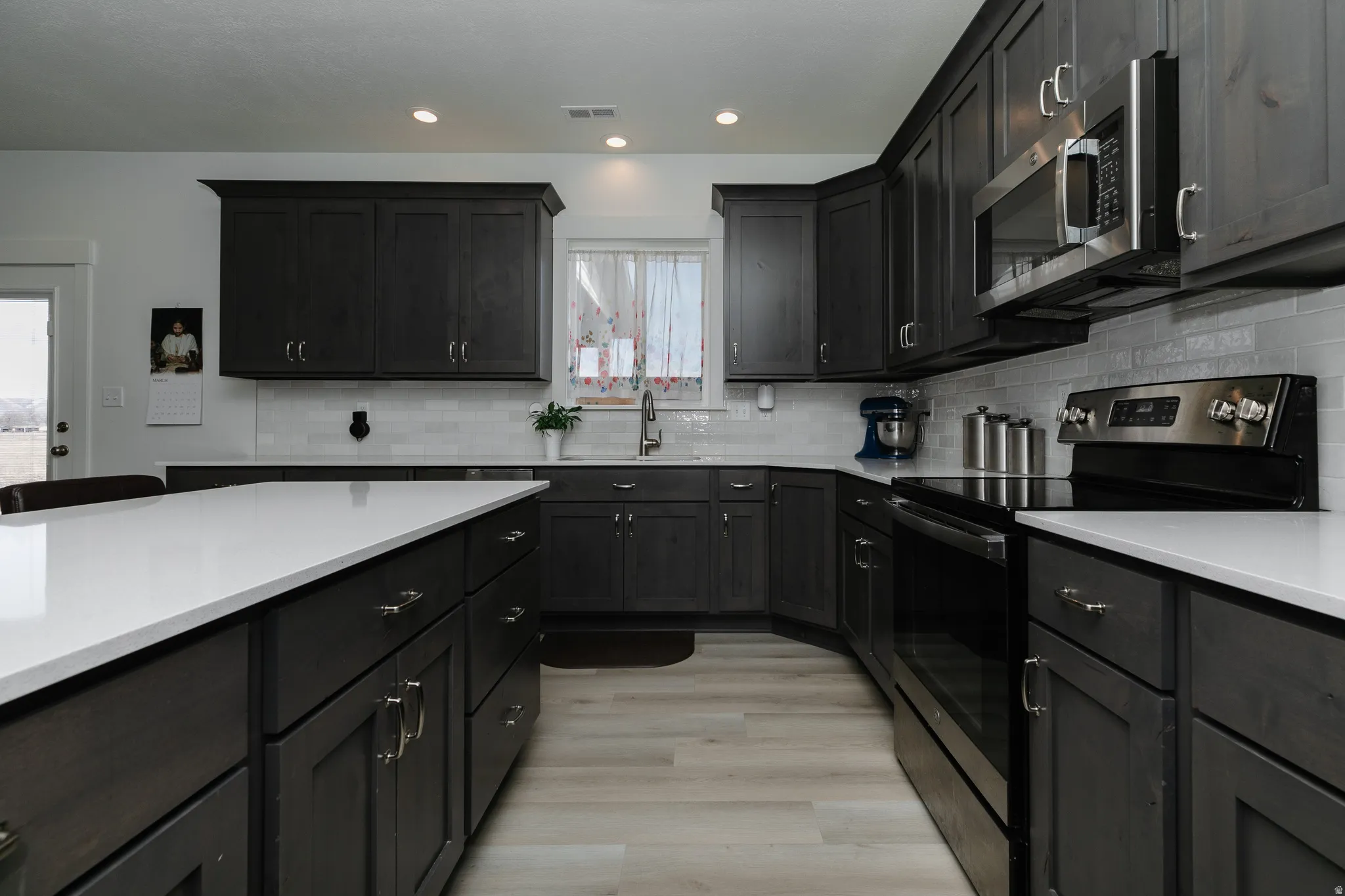 Dark wood-finish cabinetry with silver hardware, white solid-surface countertops, and light wood-finish flooring