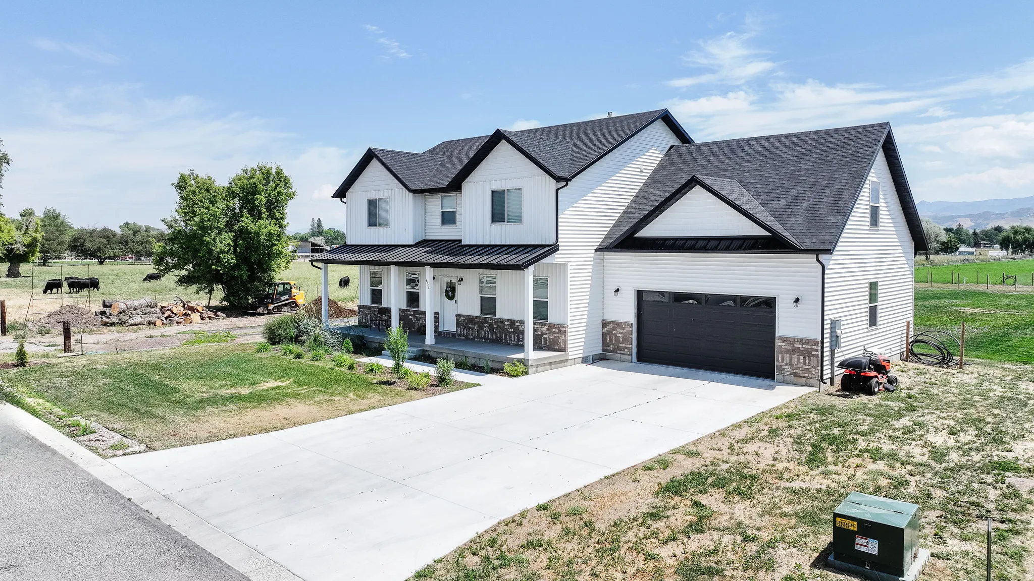 Contemporary two-story exterior with white siding, dark gabled roof, stone accents, attached garage with dark door, and concrete driveway