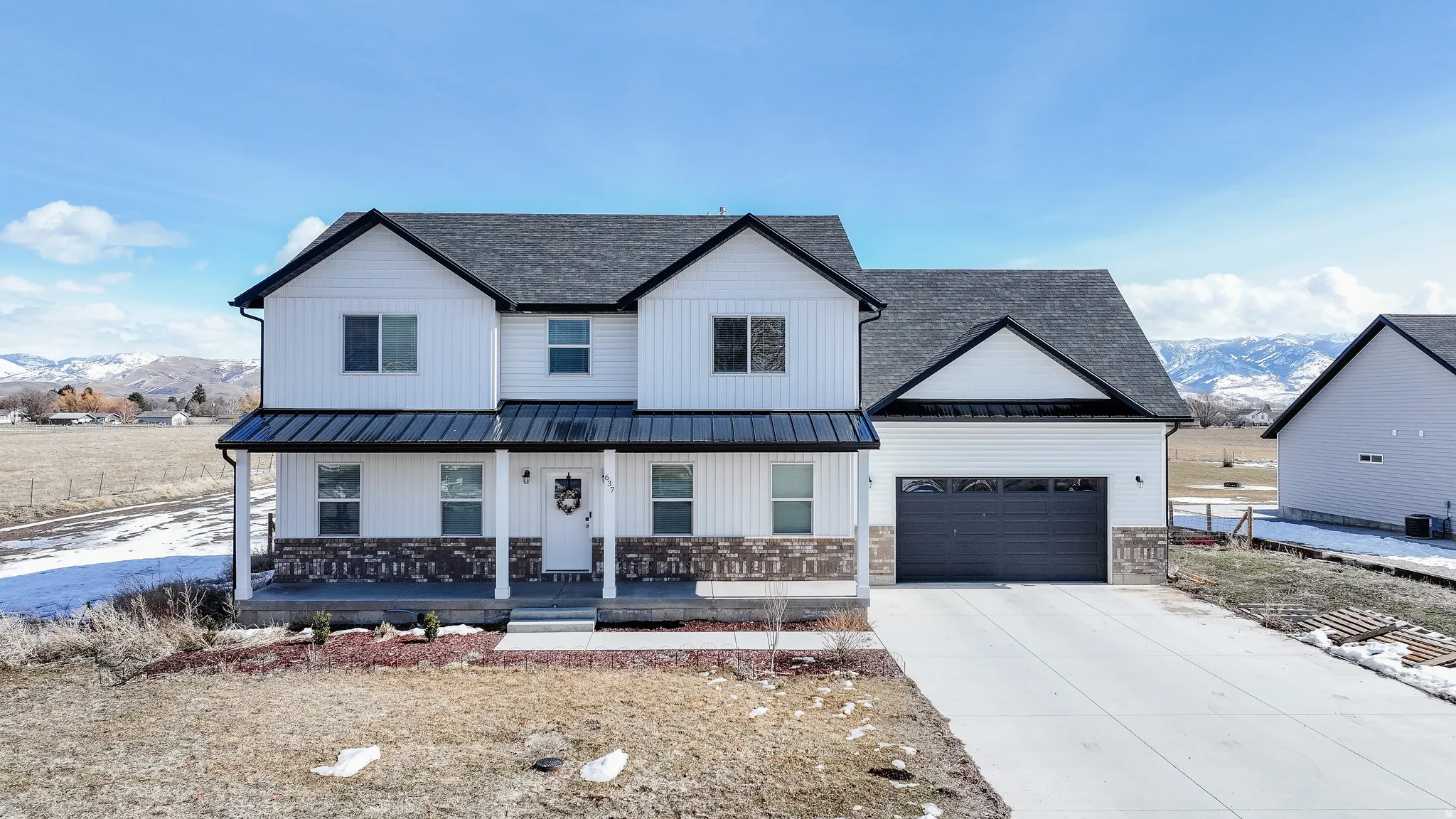 Two-story residence featuring white vertical and horizontal siding, a covered front porch with stone accents, a dark gray metal roof over the porch, and an attached garage with a dark gray door