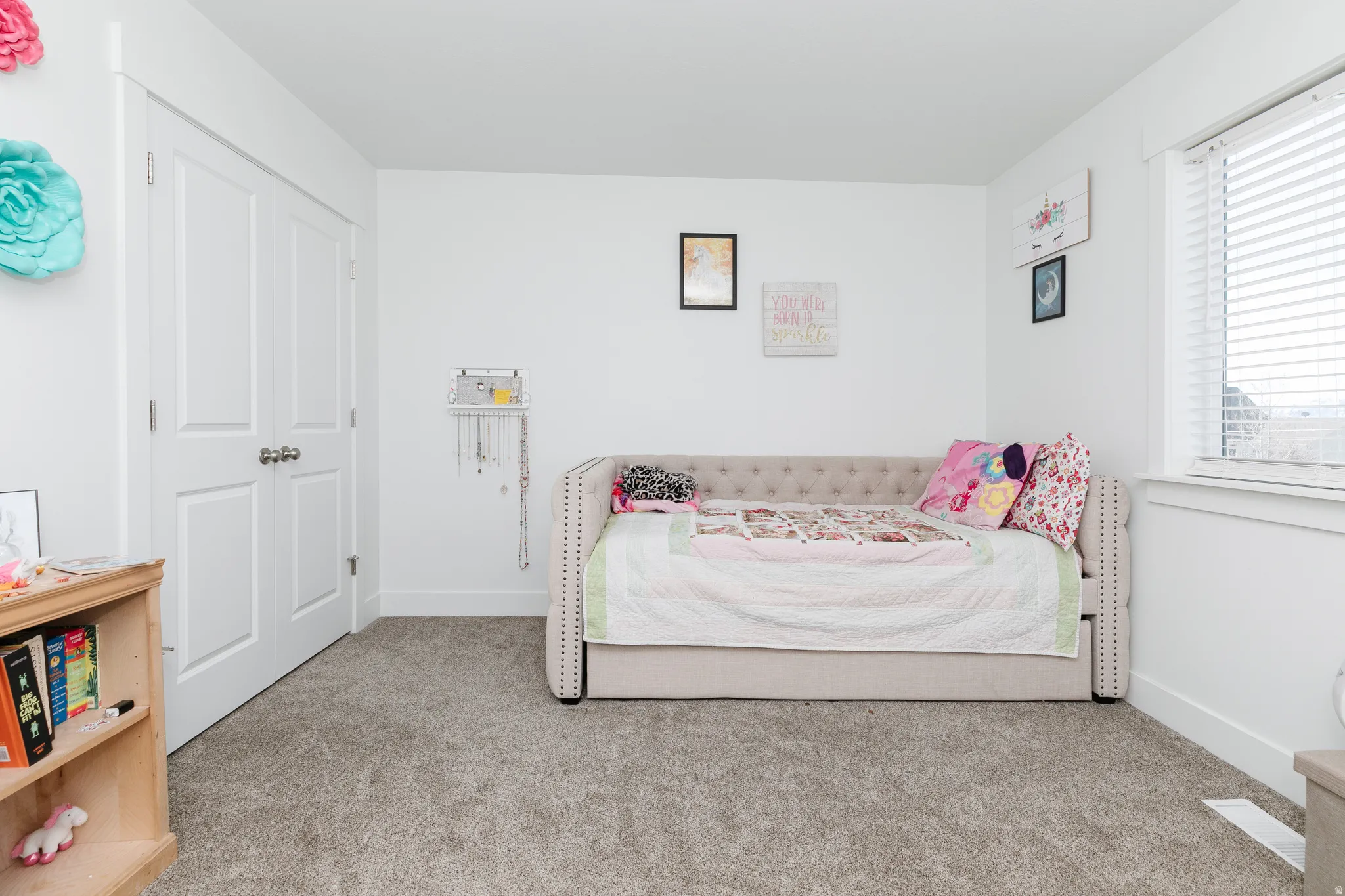 Plush carpet flooring, white painted walls, and a large window with blinds
