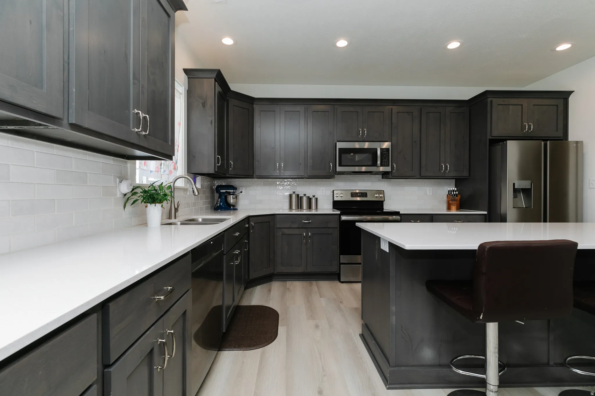 Kitchen featuring wood-finish cabinetry, white countertops, a subway tile backsplash, stainless steel appliances, and an island with countertop seating