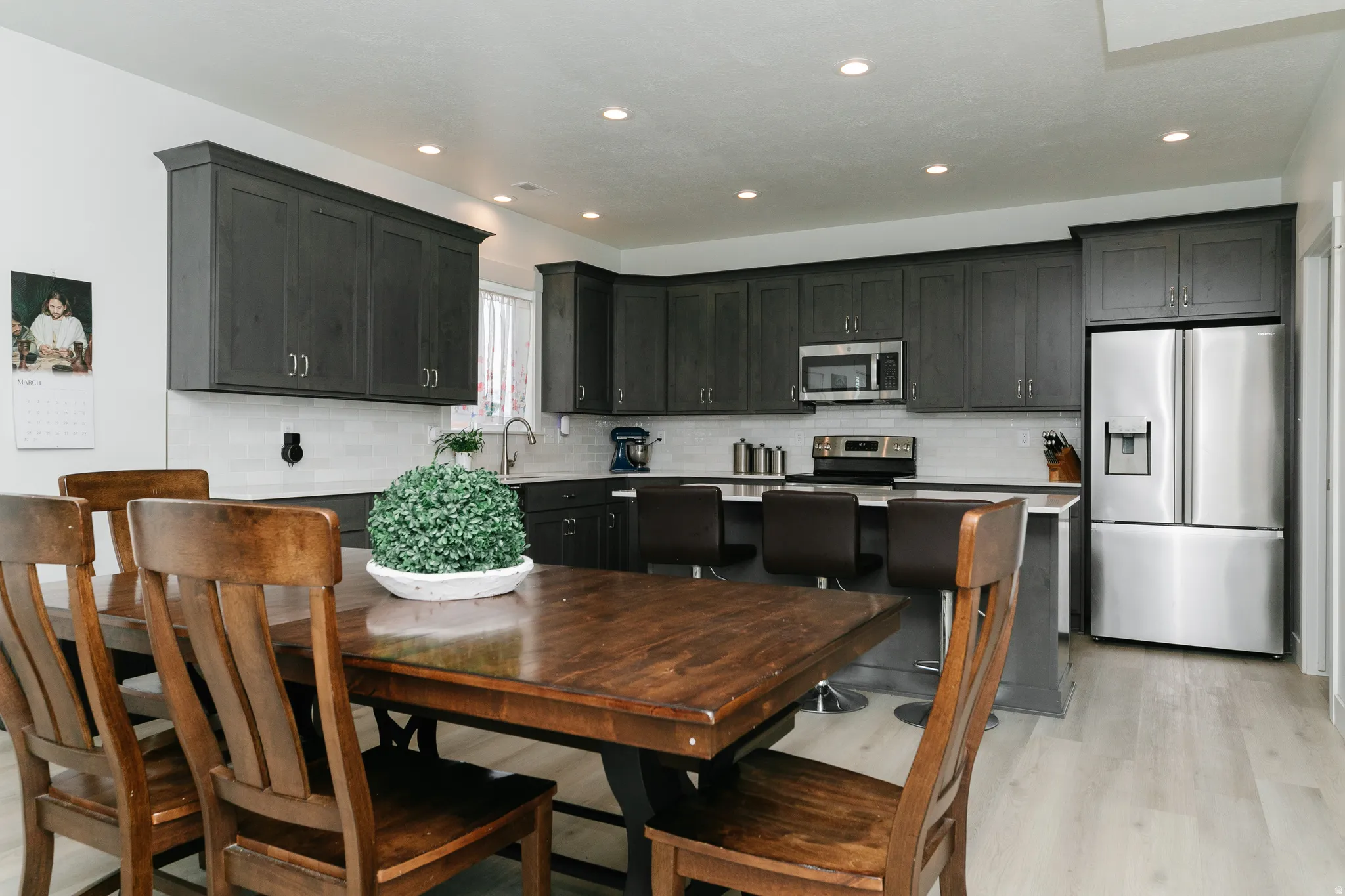 Kitchen featuring dark wood cabinetry, white subway tile backsplash, stainless steel appliances, a center island with seating, and light wood-finish flooring