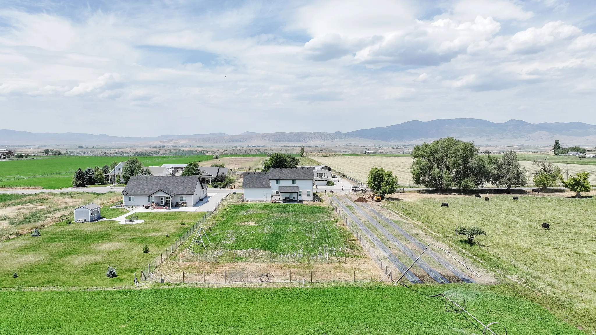 Expansive land featuring a two-story residence, a single-story residence, multiple outbuildings, and distant mountain scenery