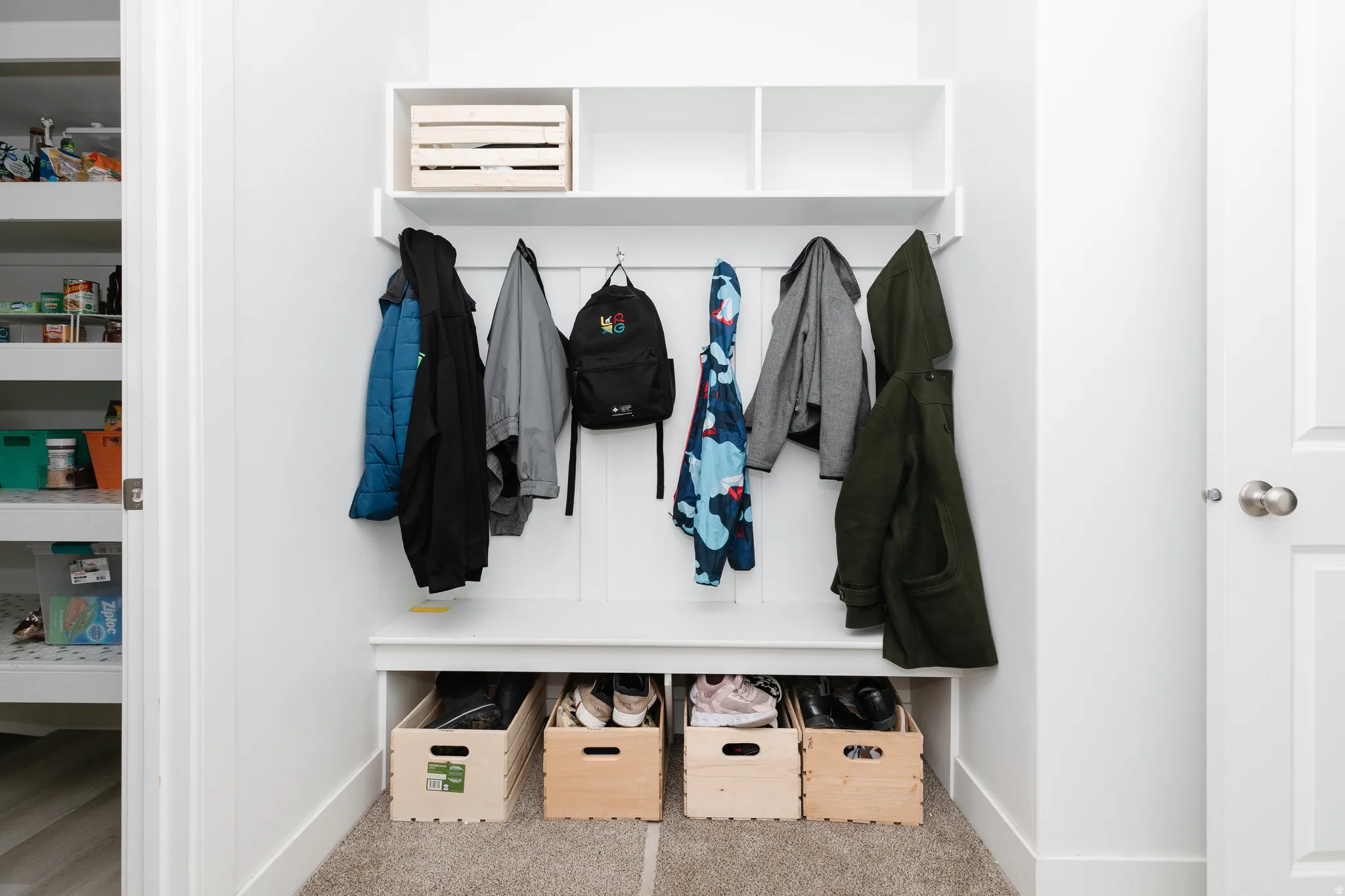Built-in white storage bench with open shelving, wall-mounted hooks, and carpeted flooring
