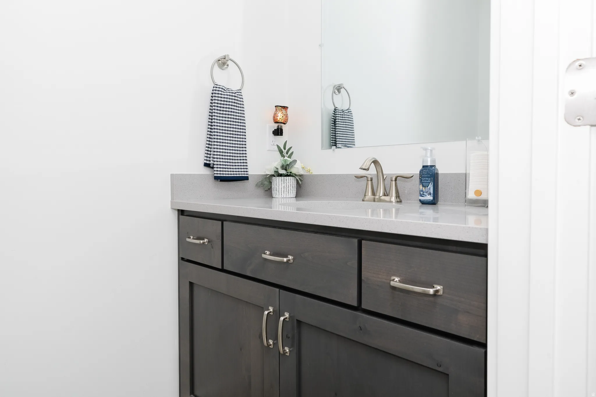 Dark wood-finish vanity with brushed nickel hardware, light-toned countertop, integrated sink, and wall-mounted sconce