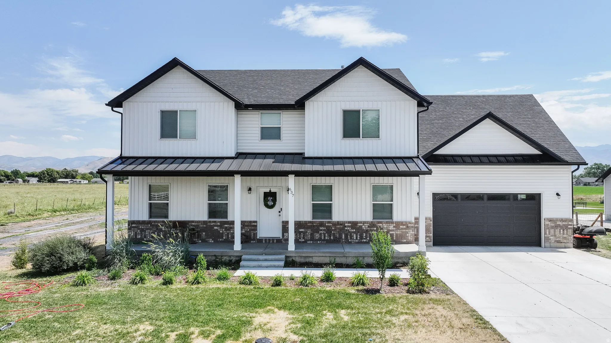 Modern farmhouse exterior featuring white vertical and horizontal siding, dark grey shingle roofing, a covered porch with a dark metal awning, and a two-car garage with a dark panel door