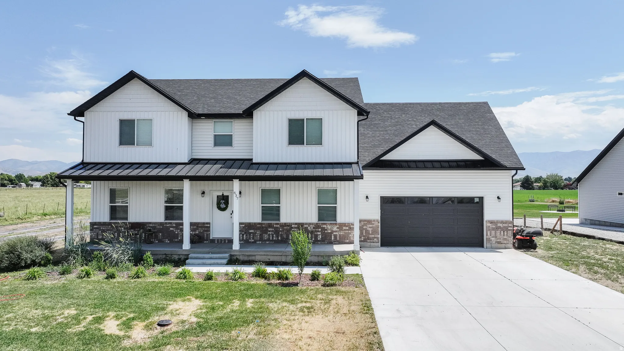 Two-story residence featuring white board-and-batten siding with stone veneer accents, a dark shingle roof, and a covered front porch