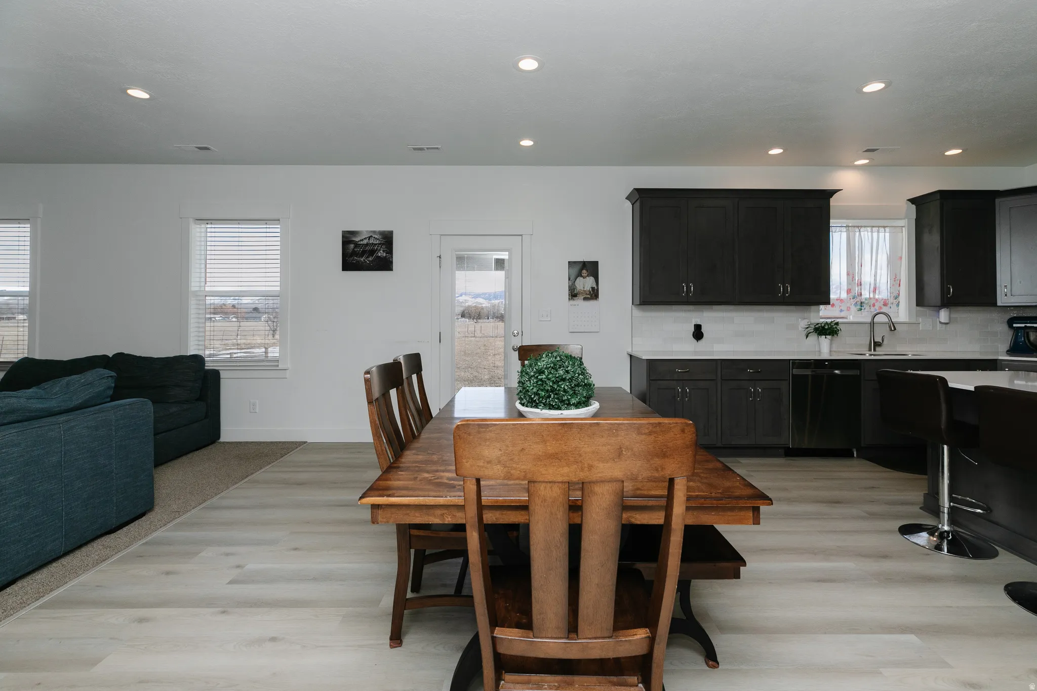 Recessed lighting illuminates the open-concept living space, featuring wood-finish flooring, dark wood-finish cabinetry, and a white subway tile backsplash