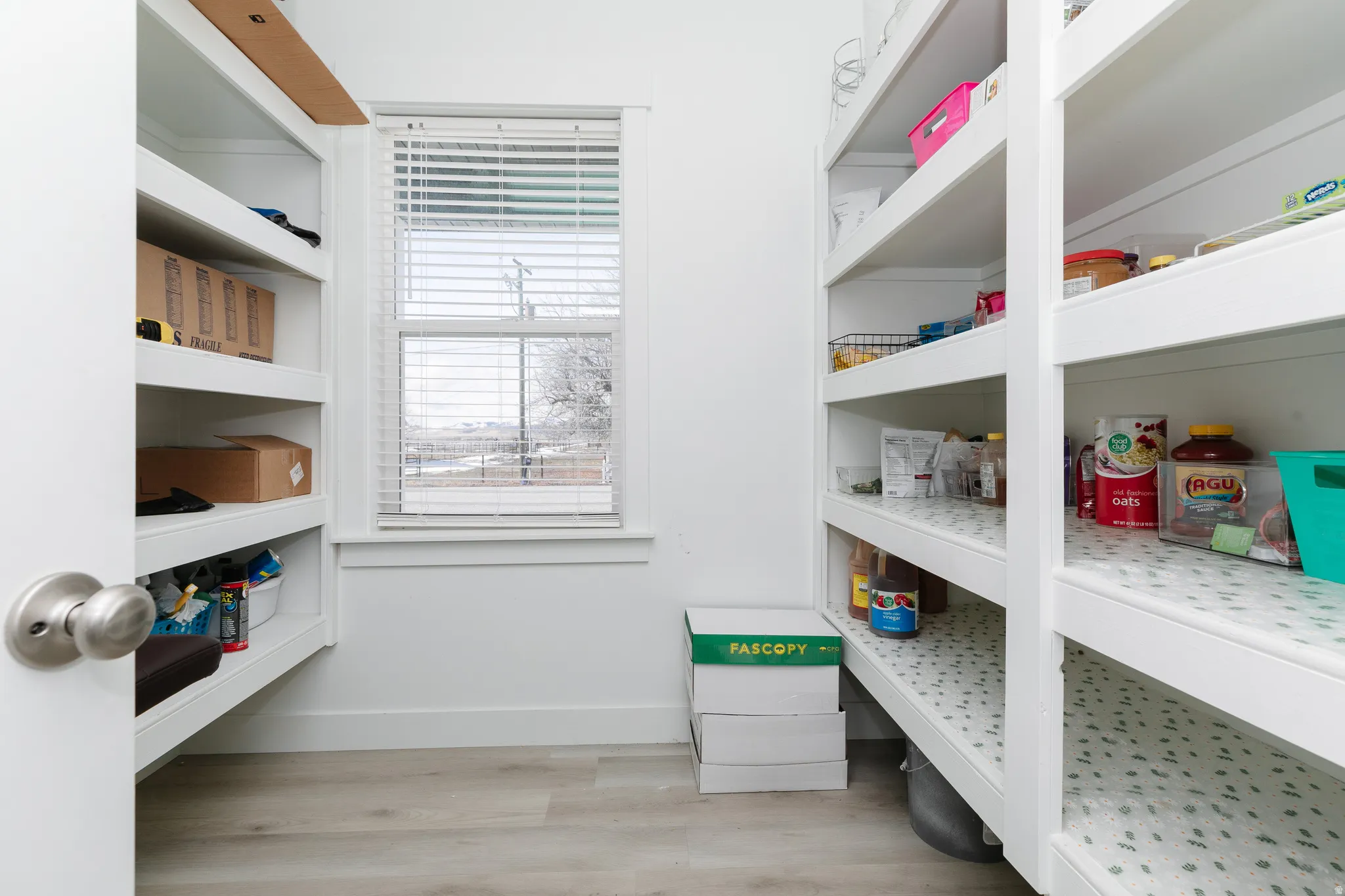 Built-in shelving for storage, single-hung window with blinds, and light wood-finish flooring