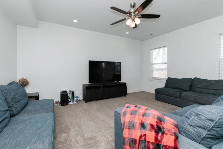 Carpeted living space with a ceiling fan, recessed lighting, and multiple windows