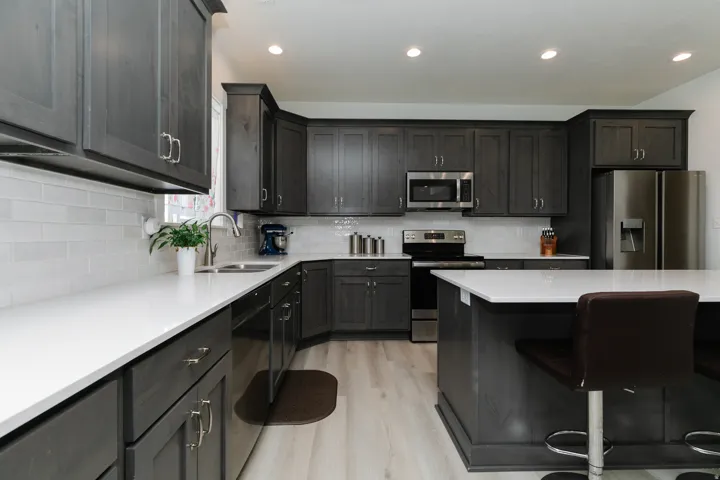 Kitchen featuring wood-finish cabinetry, white countertops, a subway tile backsplash, stainless steel appliances, and an island with countertop seating