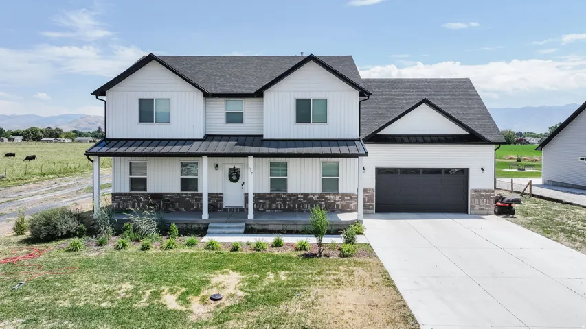 Two-story residence featuring white vertical and horizontal siding, a covered front porch with stone facade, a dark gray garage door, and a concrete driveway
