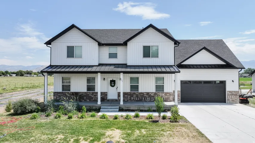 Modern farmhouse exterior featuring white vertical and horizontal siding, dark grey shingle roofing, a covered porch with a dark metal awning, and a two-car garage with a dark panel door