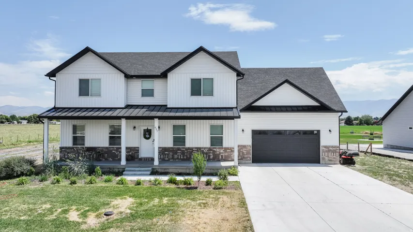 Two-story residence featuring white board-and-batten siding with stone veneer accents, a dark shingle roof, and a covered front porch