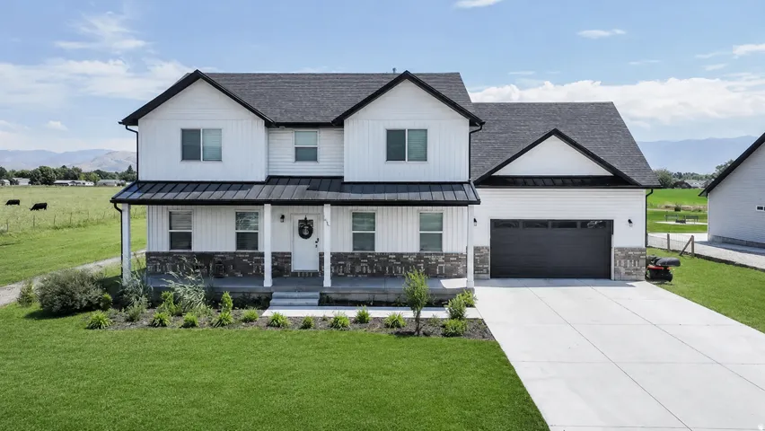 Two-story residence featuring white board-and-batten siding, a dark shingle roof, a covered front porch with stone accents, and an attached two-car garage
