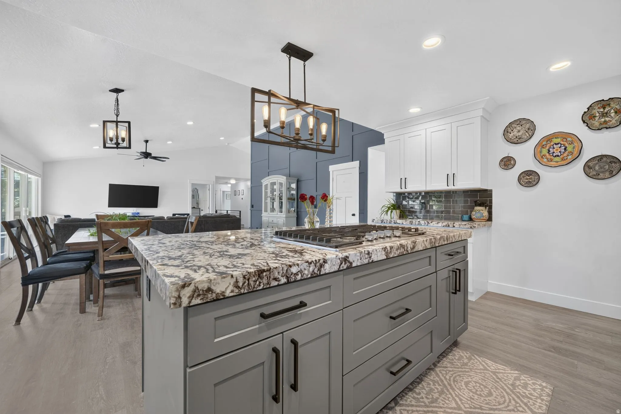 Kitchen island with built-in gas cooktop, granite-style countertop, gray shaker cabinetry, and black hardware