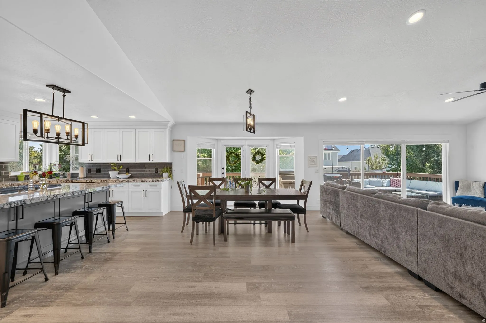 Open-concept living space featuring vaulted ceilings, wood-finish flooring, a kitchen island with stone countertop, and glass sliding doors leading to an outdoor deck