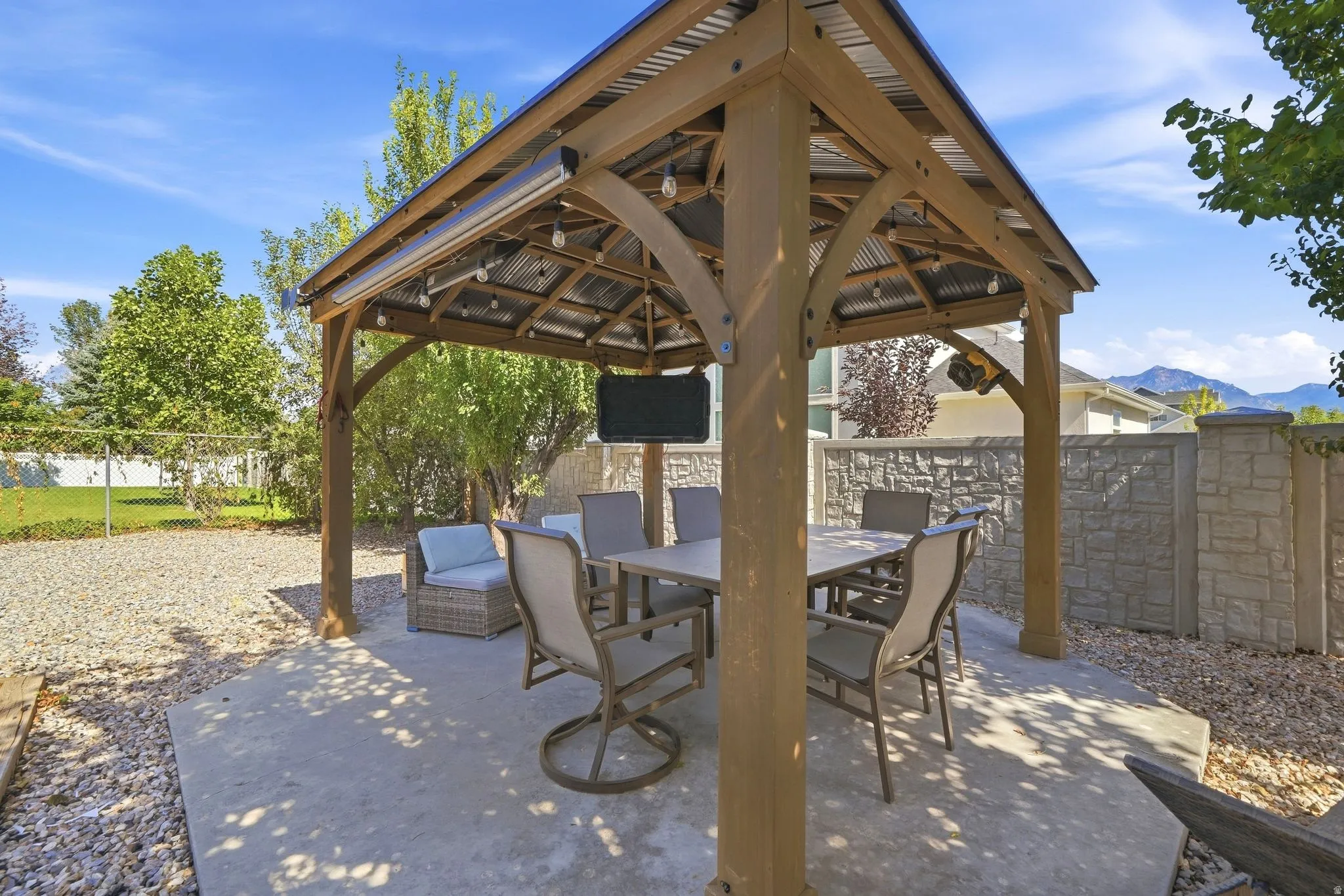 Outdoor gazebo with a corrugated metal roof, a concrete patio, string lighting, and a stone-look perimeter fence