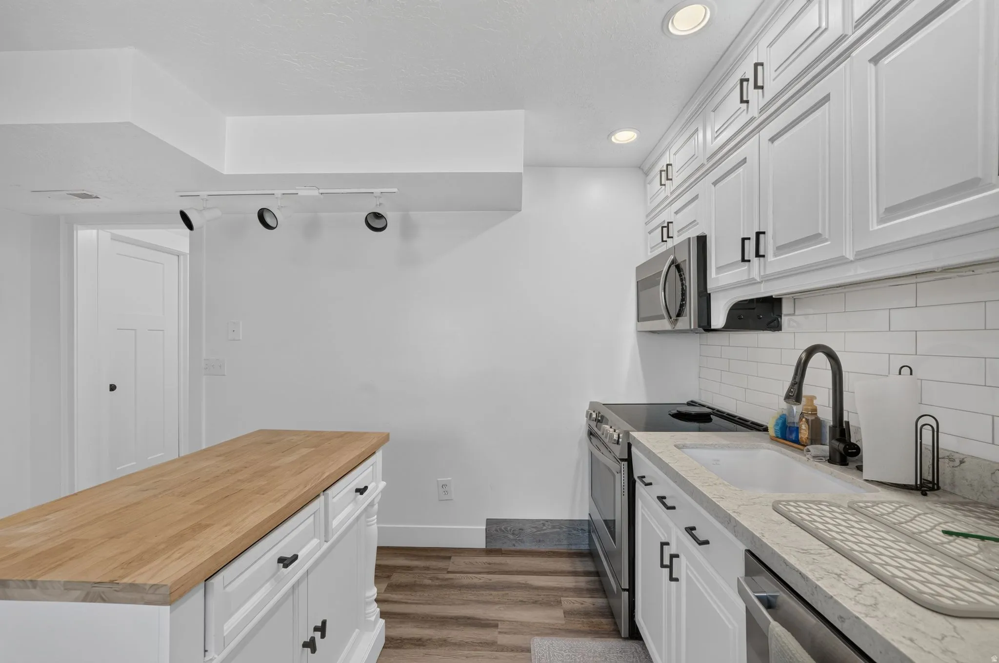 White cabinetry with dark hardware, wood-finish flooring, and a subway tile backsplash