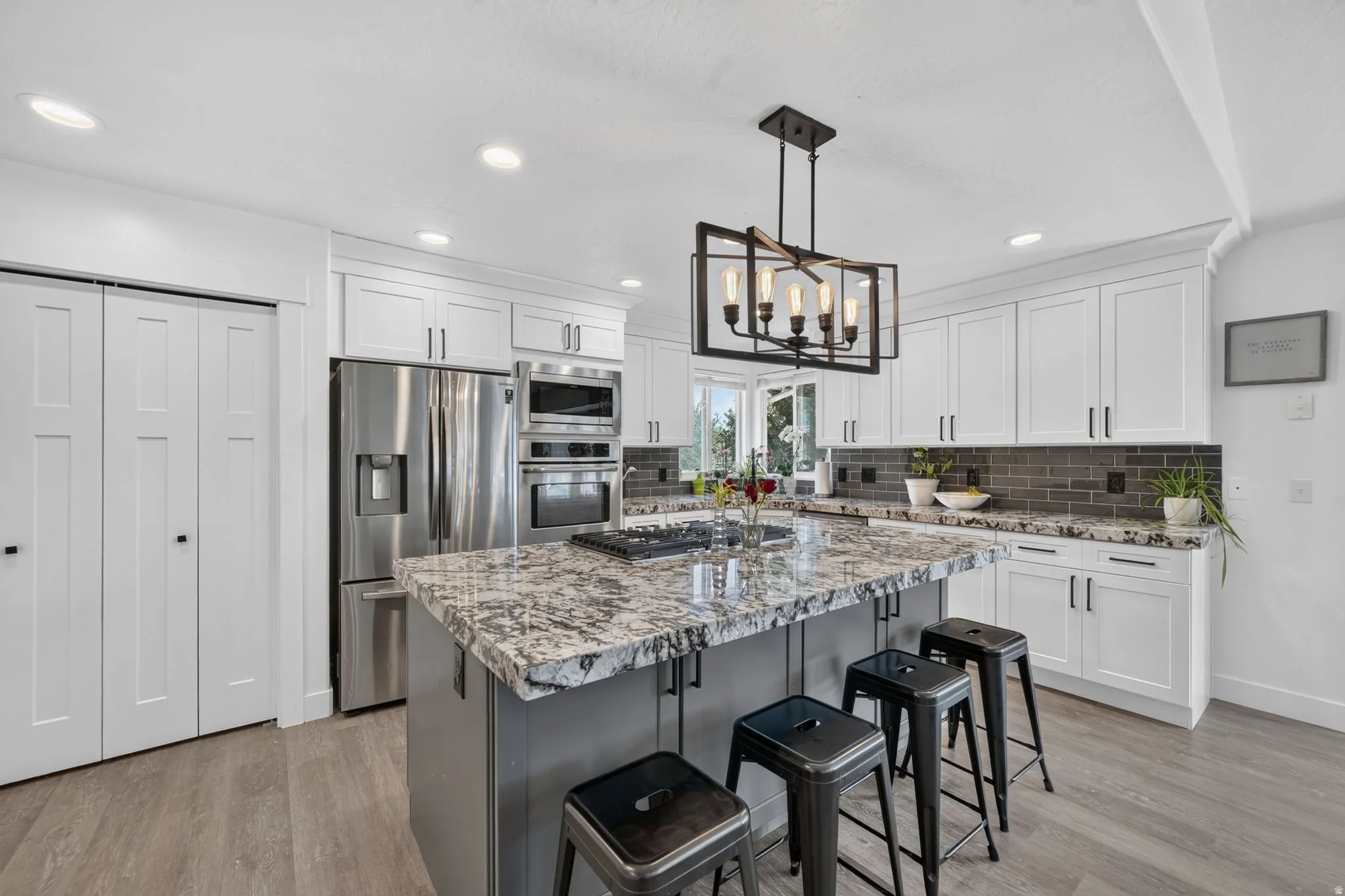 Expansive kitchen featuring wood-finish flooring, white shaker cabinetry, a large kitchen island with a stone-finish countertop, and stainless steel appliances