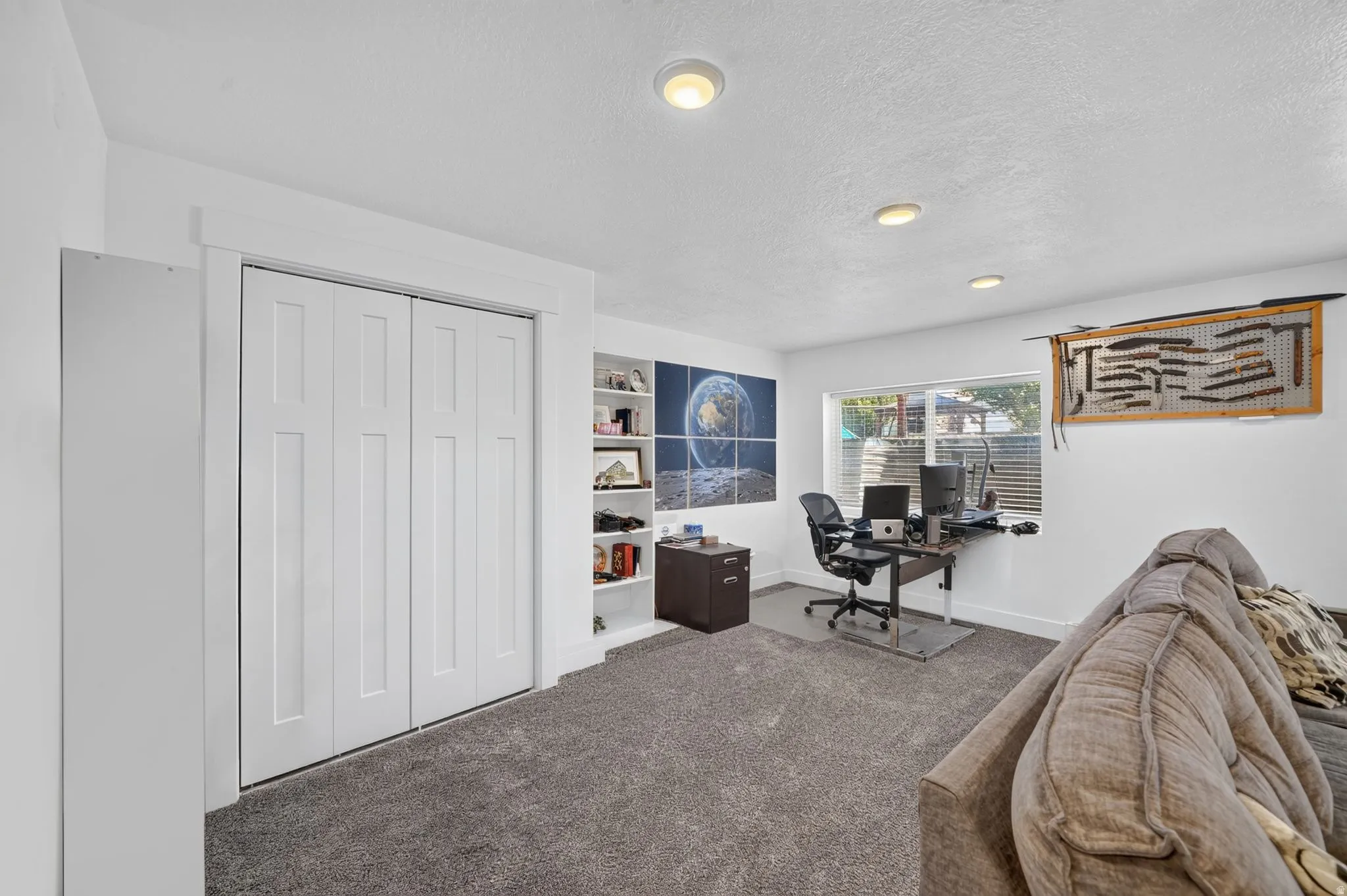 Recessed lighting, built-in shelving, white trim, grey carpeting, and a window for natural light