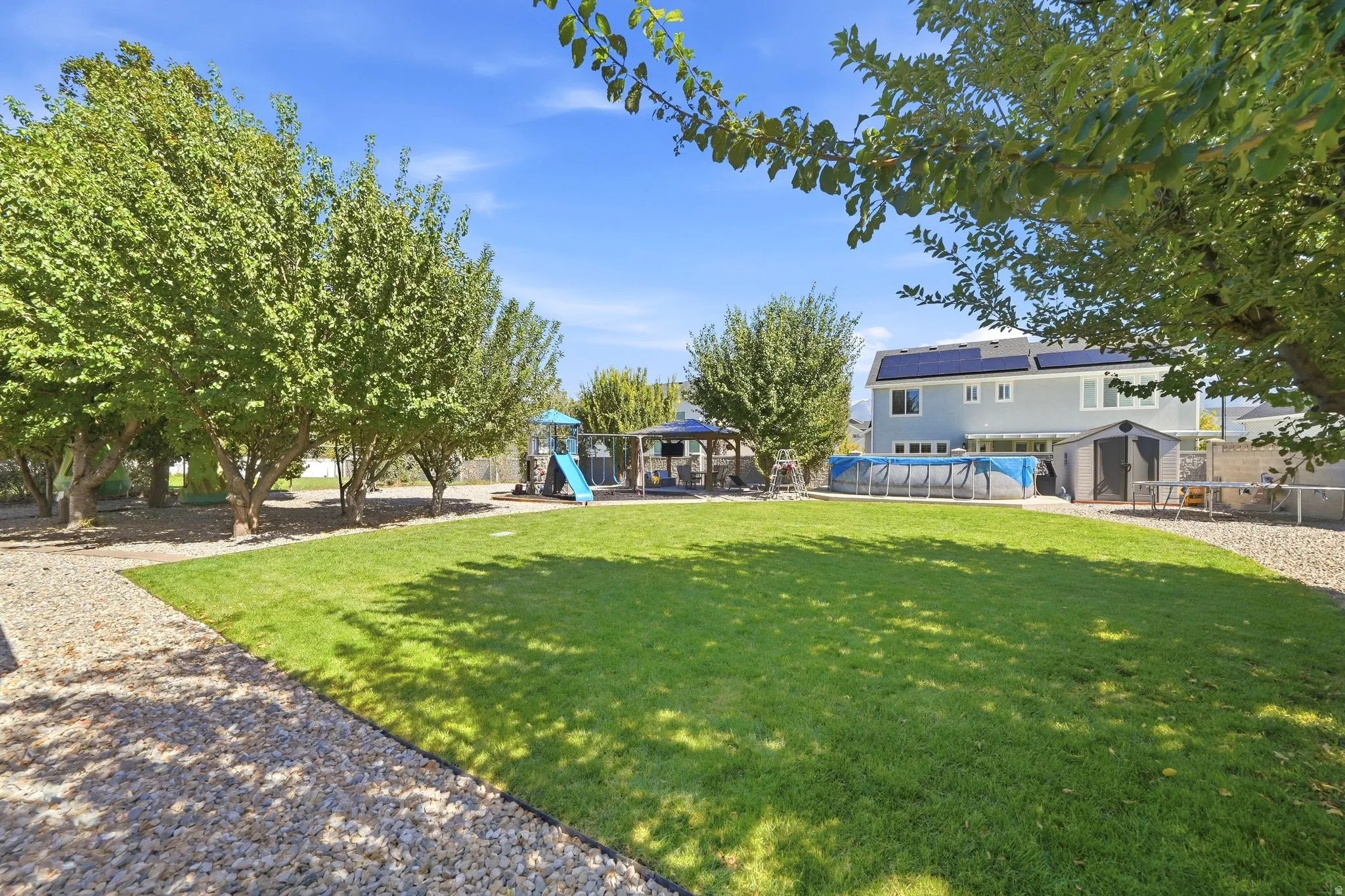 Expansive backyard featuring a manicured lawn, established trees, and a gravel pathway