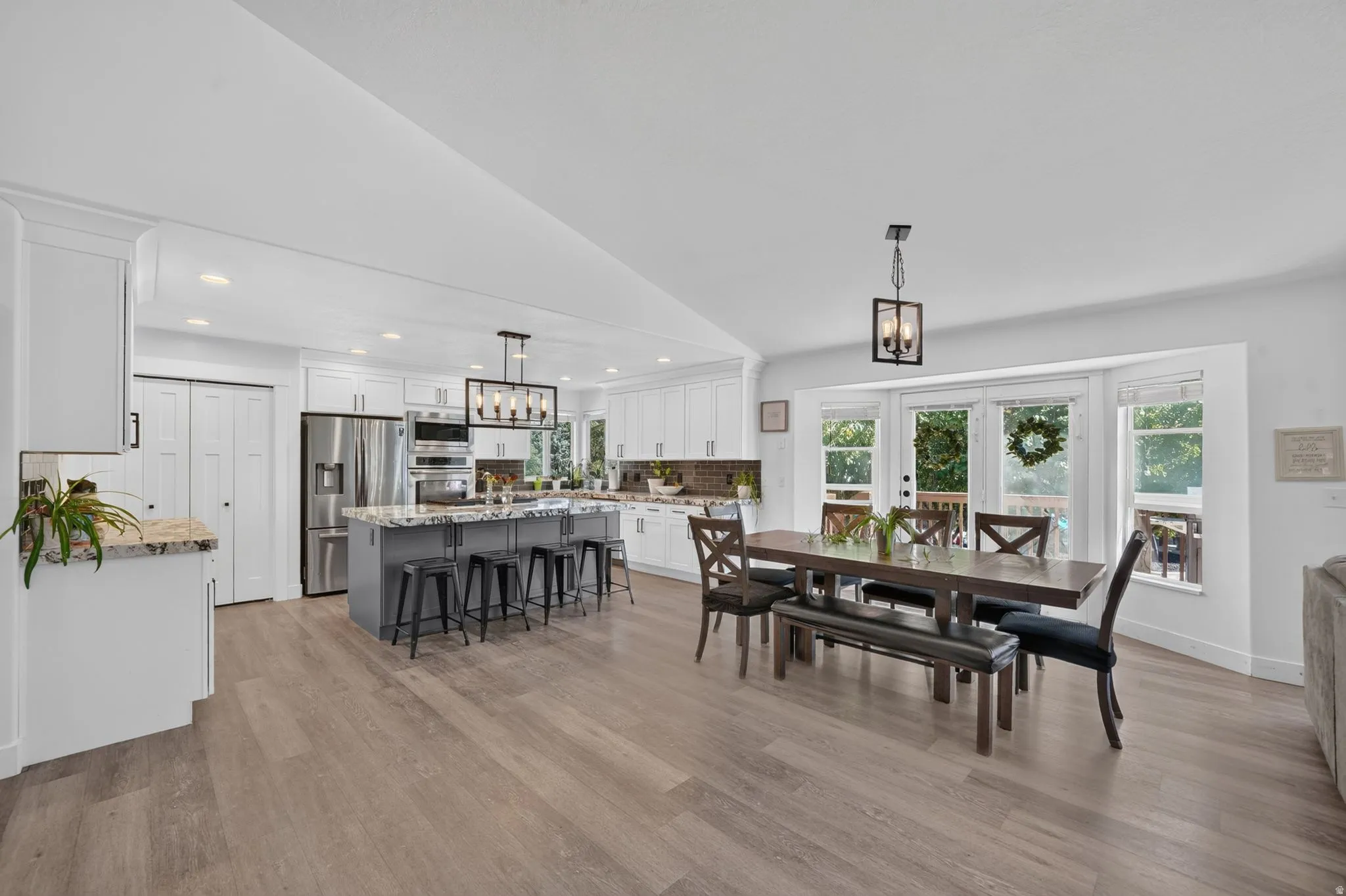 Open-concept design featuring wood-finish flooring, white cabinetry, a kitchen island with seating, a stainless steel appliance suite, and abundant natural light