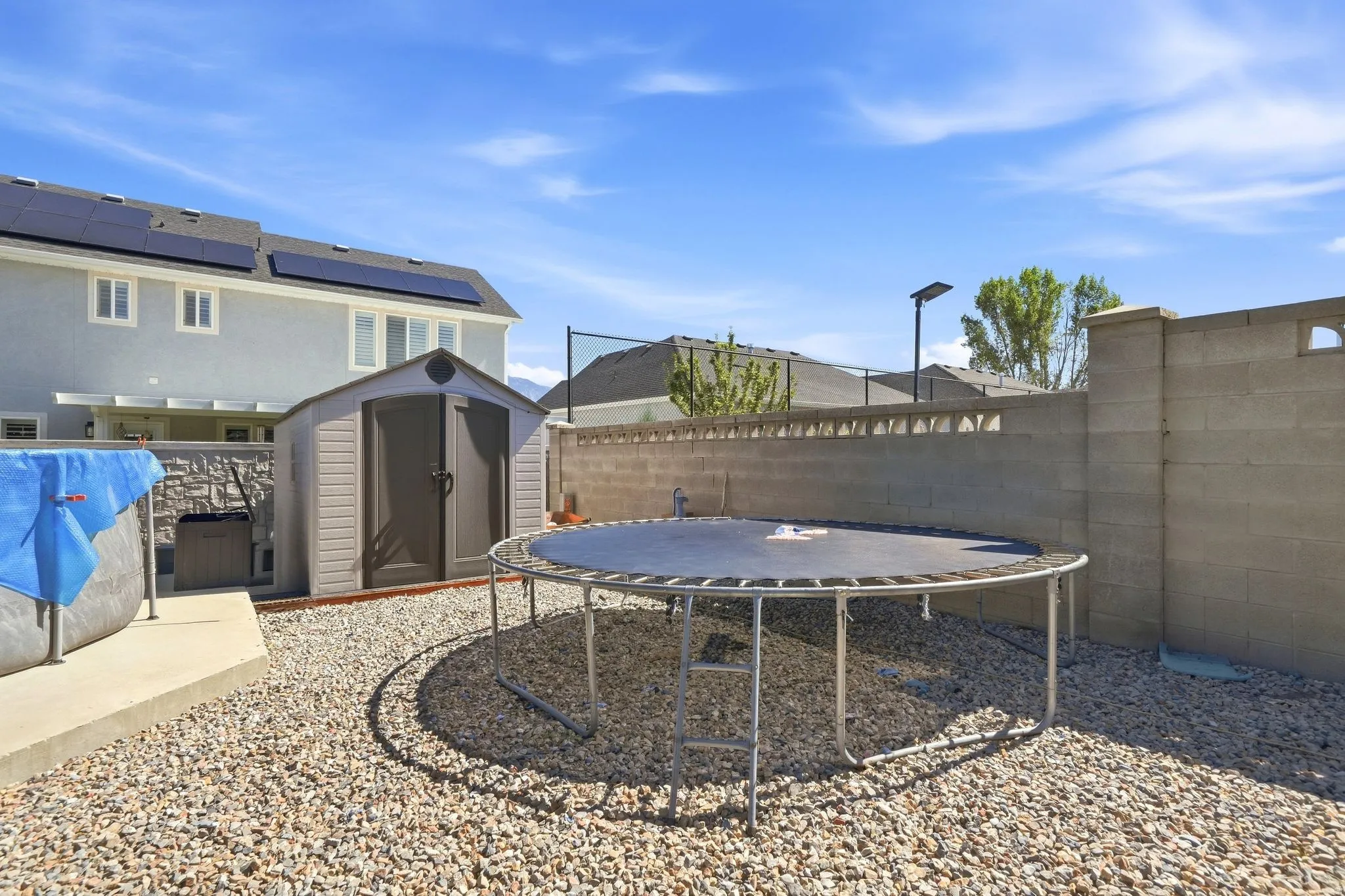 Rear exterior featuring solar panels, a storage shed, and a privacy wall