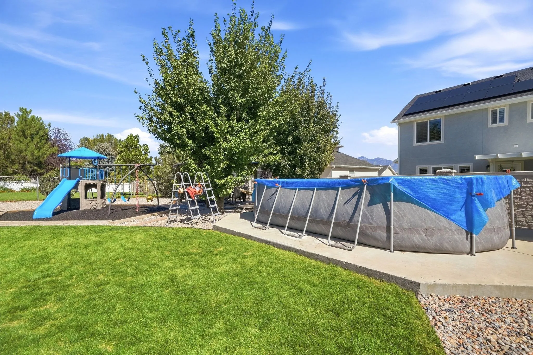 Expansive green lawn, playground structure with slide, swing set, and large above-ground pool on a concrete pad