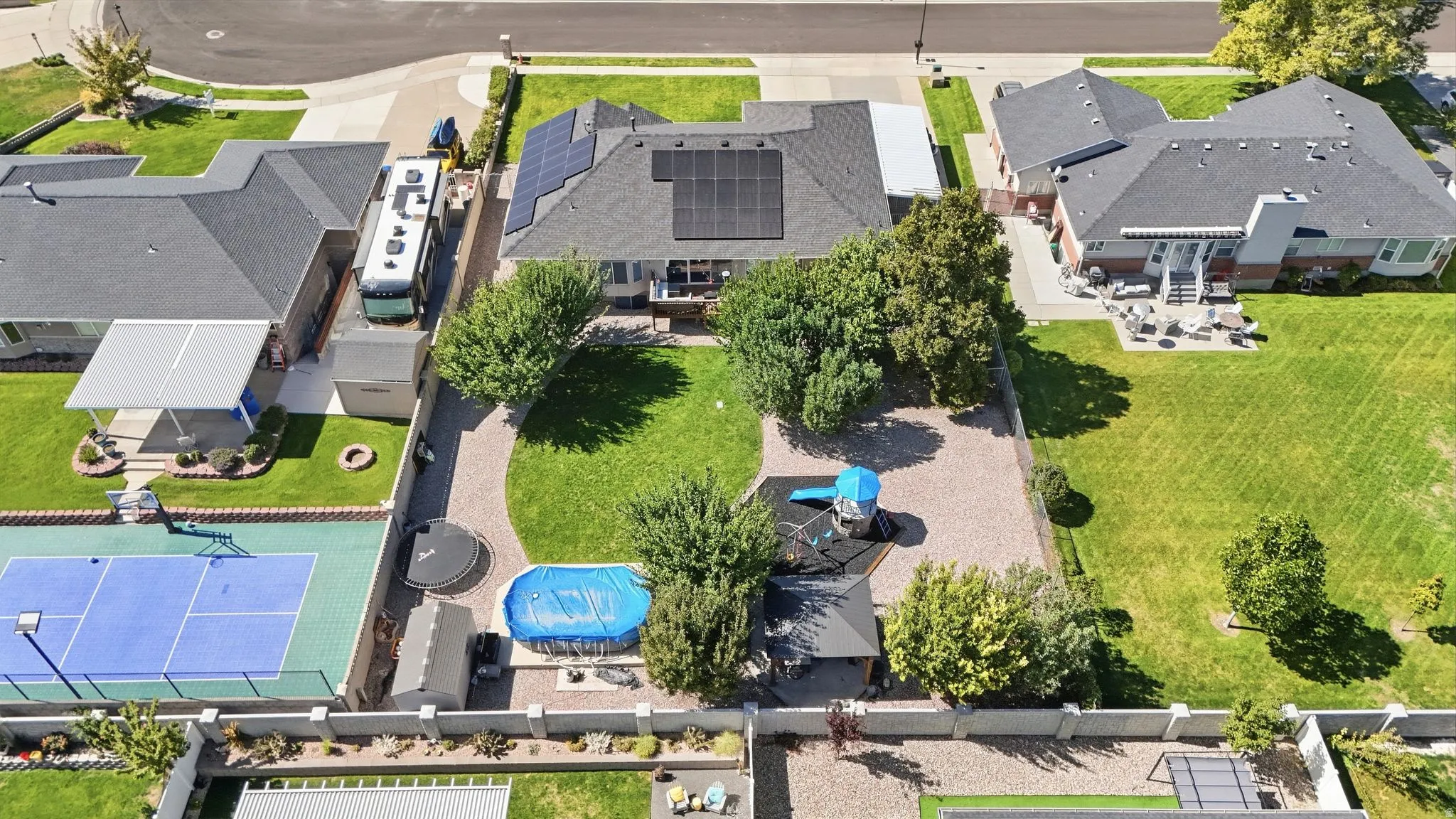 Expansive backyard featuring a manicured lawn, established trees, paved patio, and a dedicated sports court