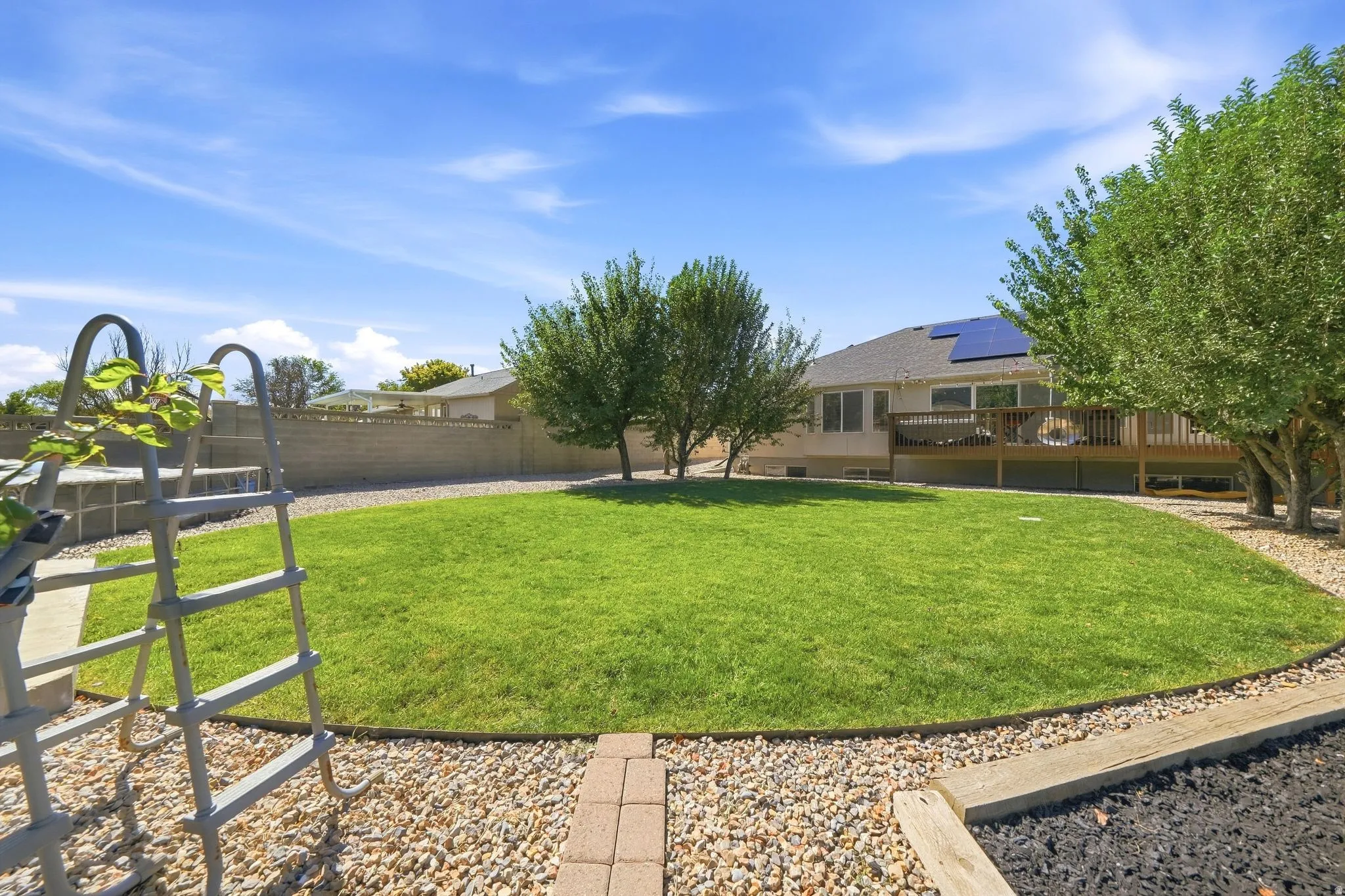 Expansive rear yard featuring a manicured lawn, established trees, and a perimeter block wall
