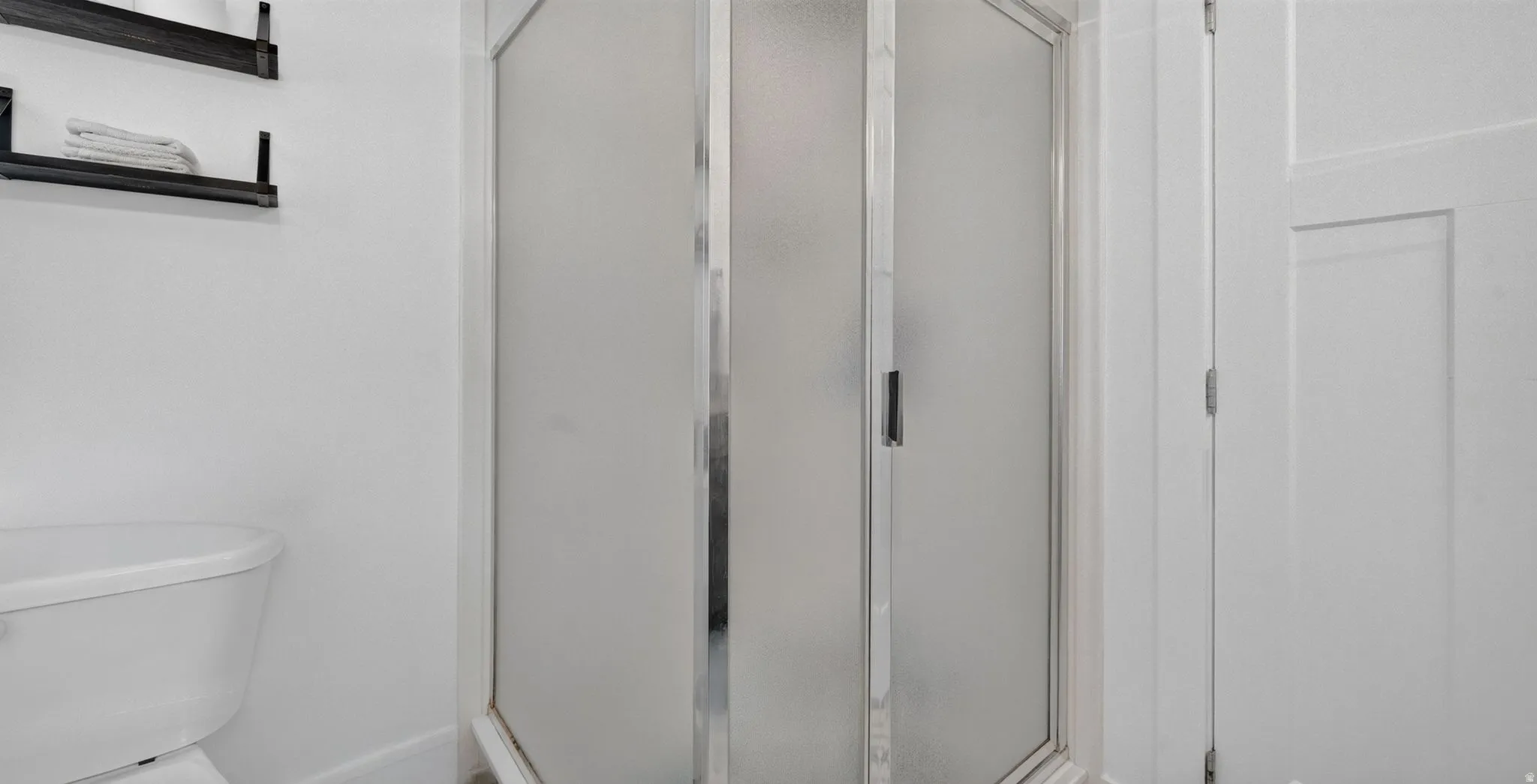 Frosted glass shower enclosure with chrome framing, adjacent to a white toilet