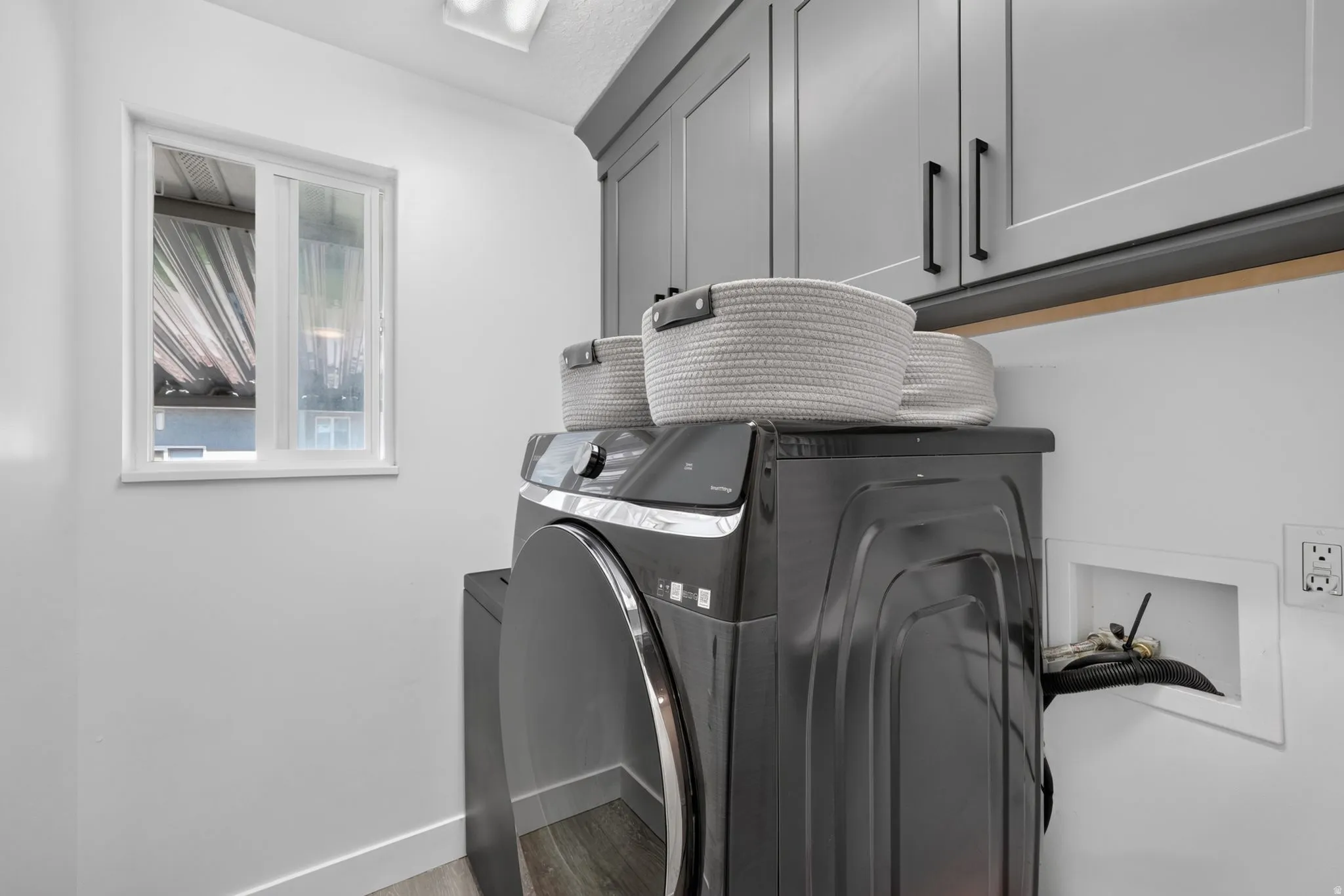 White walls, window, gray cabinetry, black cabinet hardware, and wood-finish flooring