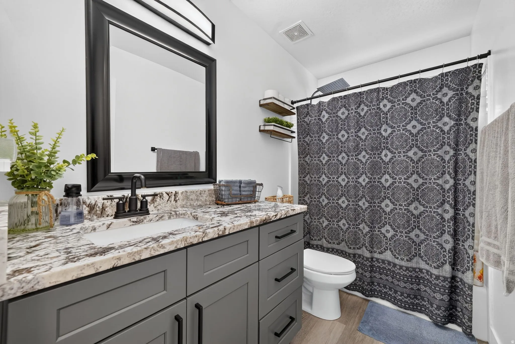 Bathroom featuring a gray vanity with black hardware, stone-finish countertop, undermount sink, and a framed mirror