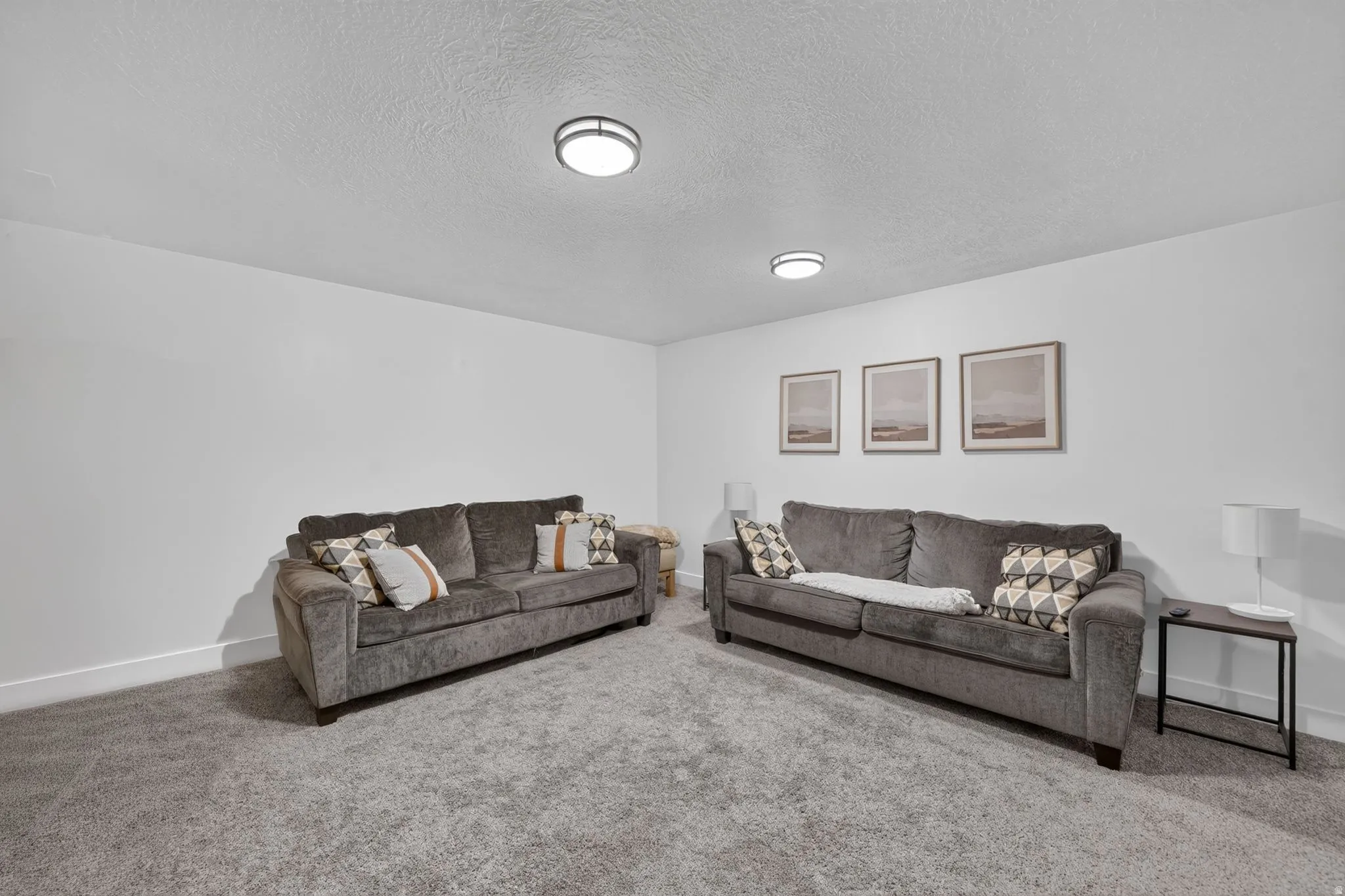 Spacious recreation room featuring dual upholstered sofas, recessed ceiling lighting, neutral carpet flooring, and framed wall art